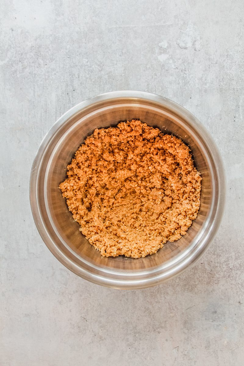 Crushed cheesecake base sits in a stainless steel bowl on a gray surface.