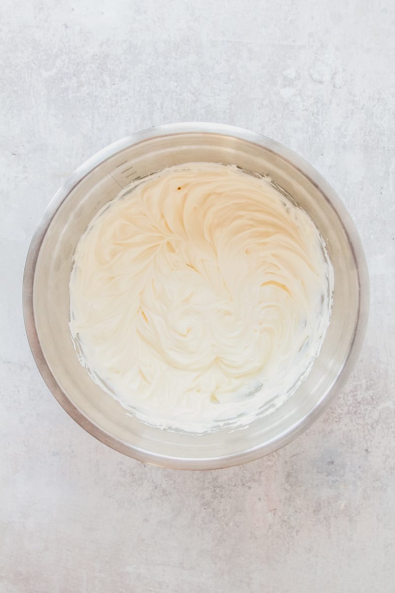 Whipped cream cheese sits in a stainless steel bowl on a gray surface.