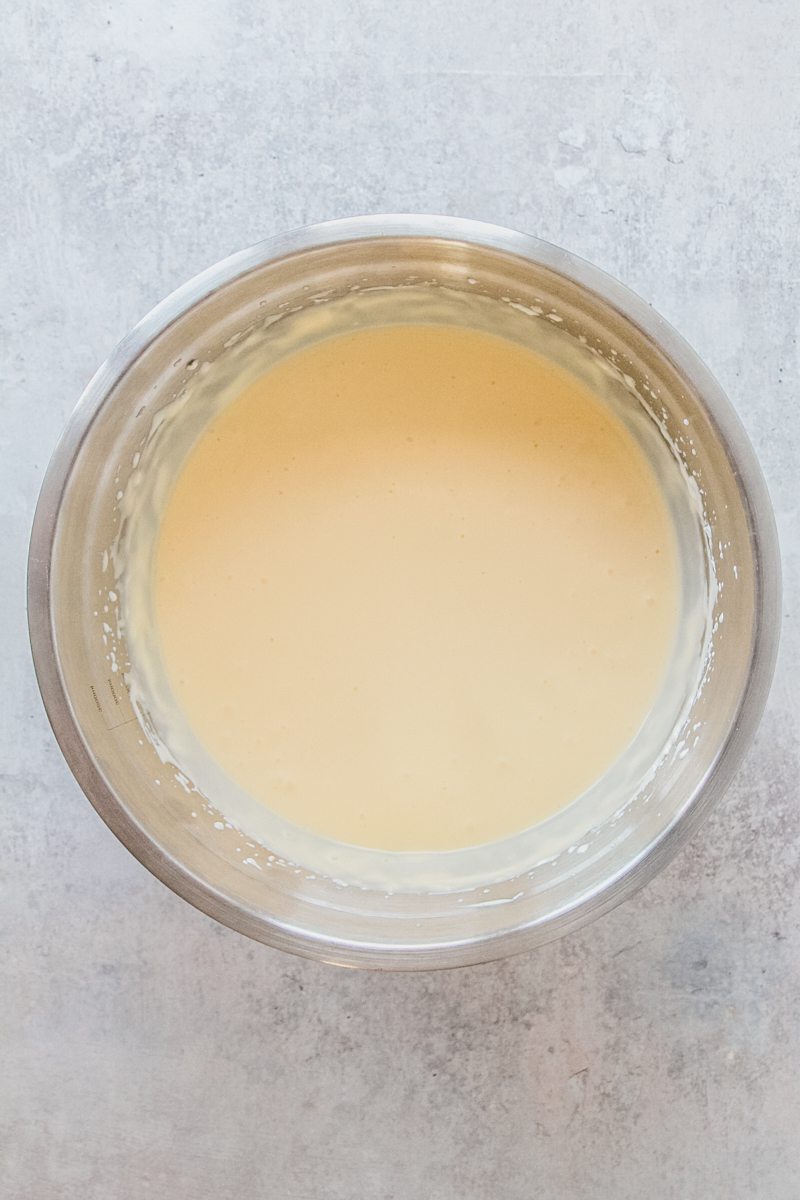 Whipped eggs and egg yolks sit in a stainless steel bowl on a gray surface.