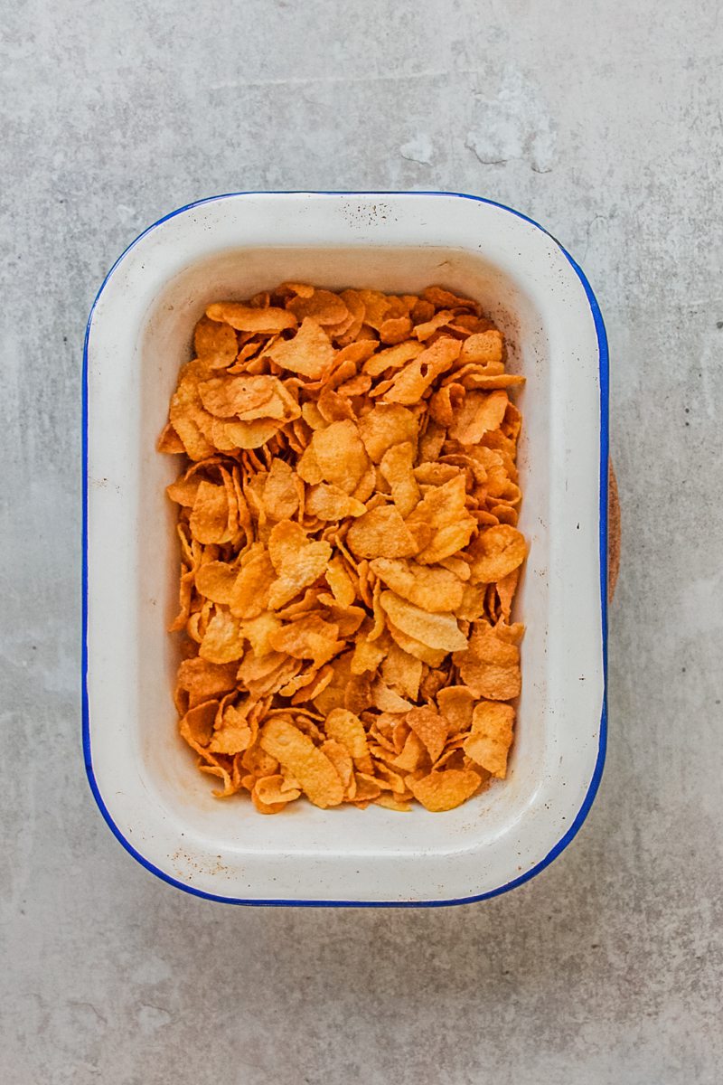Toasted cornflakes sit in an enamel dish on a gray surface.