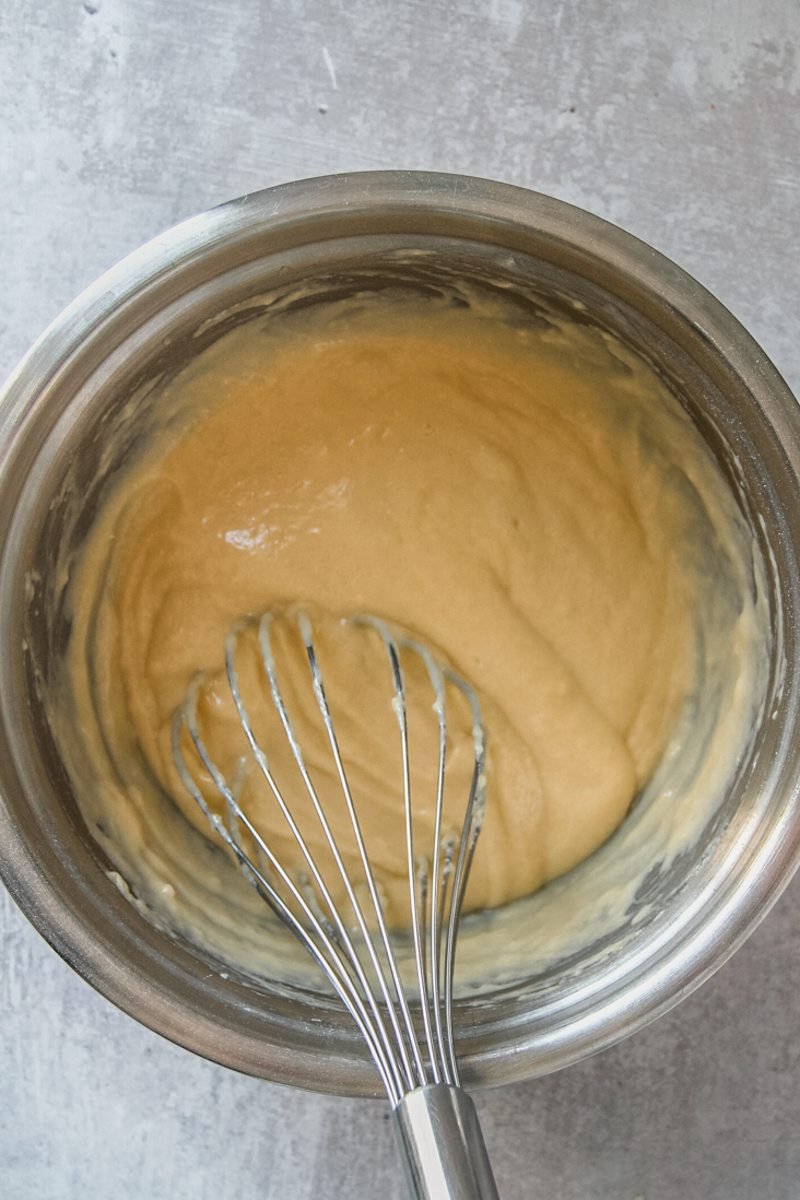 A losse cake batter sits in a round stainless steel bowl on a gray surface.