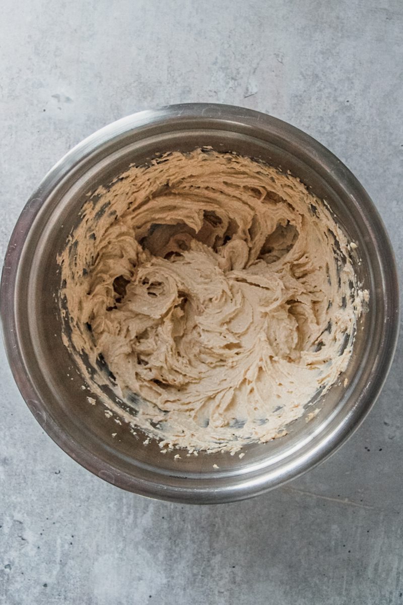Whipped butter and sugars sit in a stainless steel bowl on a gray surface.