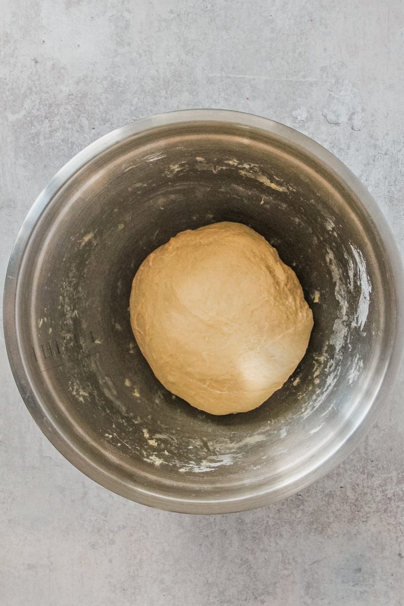 Dough sits in a stainless steel bowl on a gray surface.