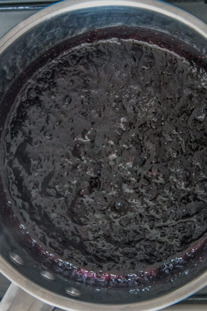 Blueberry jam sits in a stainless steel saucepan on a cooker.