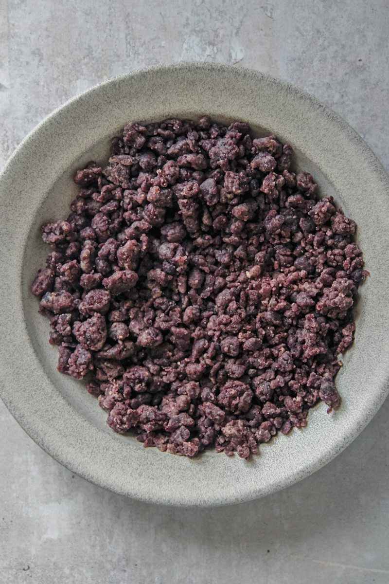 Homemade blueberry streusel sits in a shallow blue ceramic bowl on a gray surface.