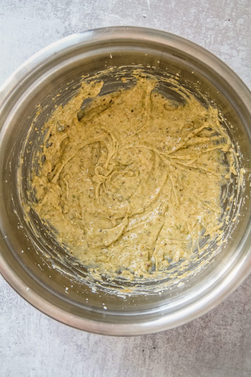 A pistachio frangipane mixture sits in a stainless steel bowl on a gray surface.