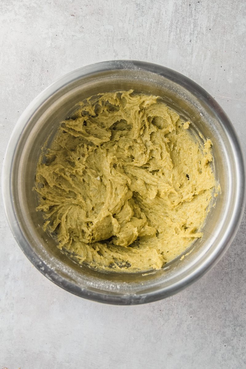 A pistachio buttercream sits whipped in a stainless steel bowl on a gray surface.