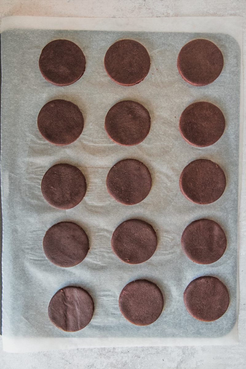 Unbaked chocolate cookies sit on a parchment lined baking tray.