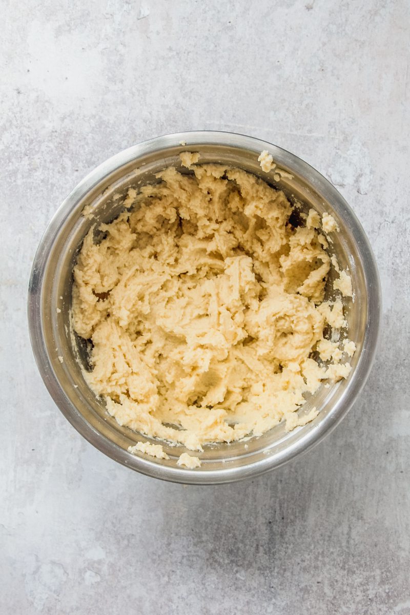 A rough cake batter sits in a stainless steel bowl on a gray surface.
