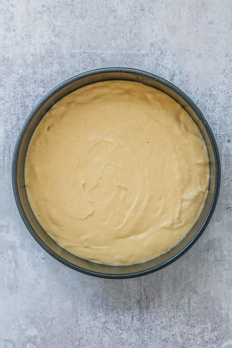 A vanilla cake batter sits in a round metal cake tin on a gray surface.