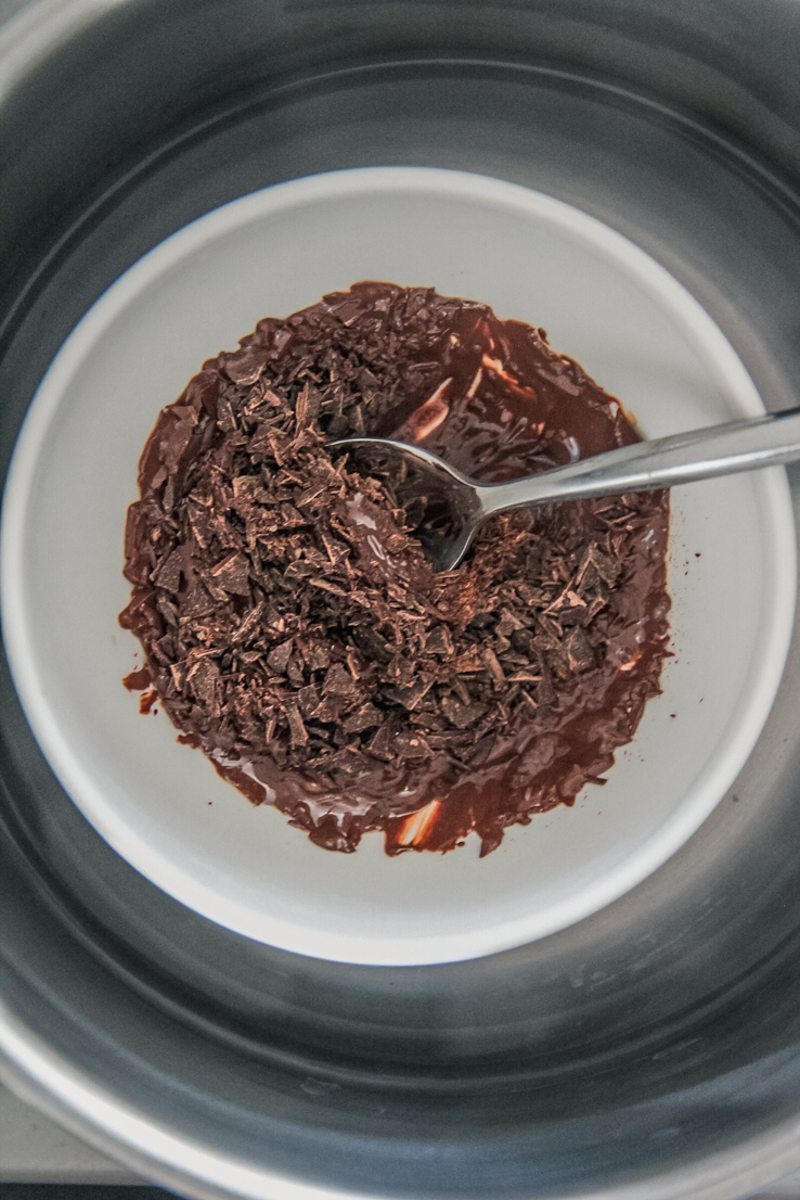 Chocolate chunks sit in a ceramic bowl in a double boiler.