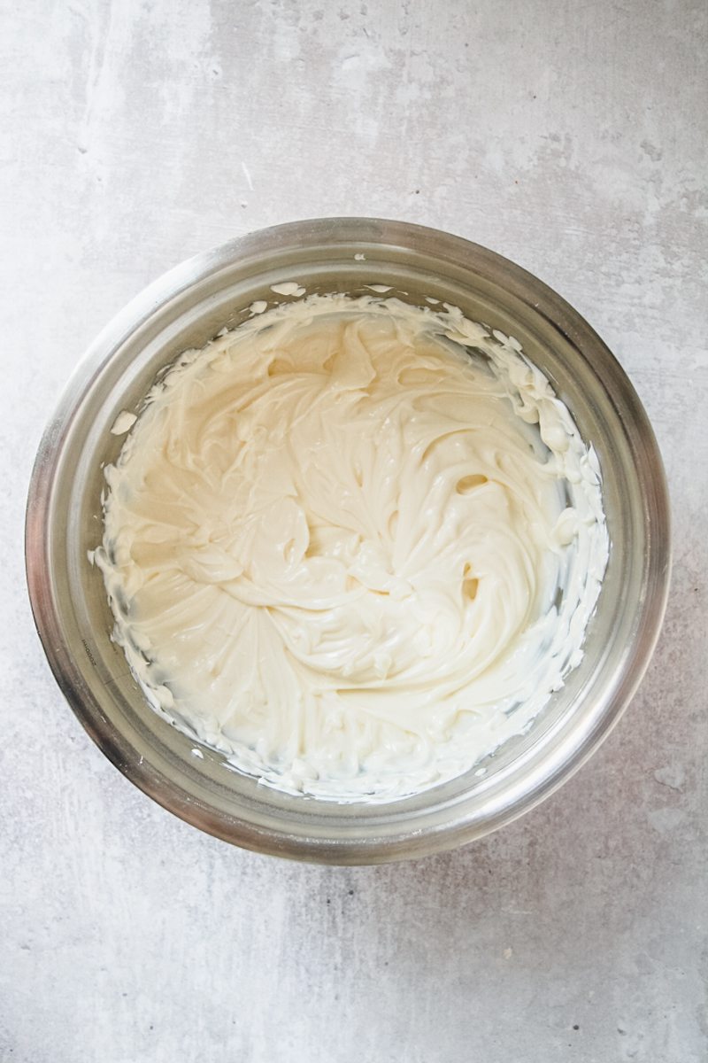 Whipped cream cheese sits in a stainless steel bowl on a gray surface.