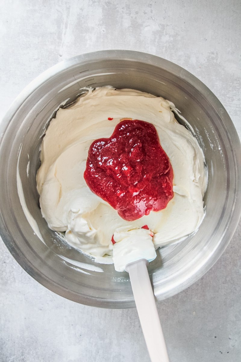 A reduced strawberry mixture sits on top of a whipped cream mixture in a stainless steel bowl on a gray surface.