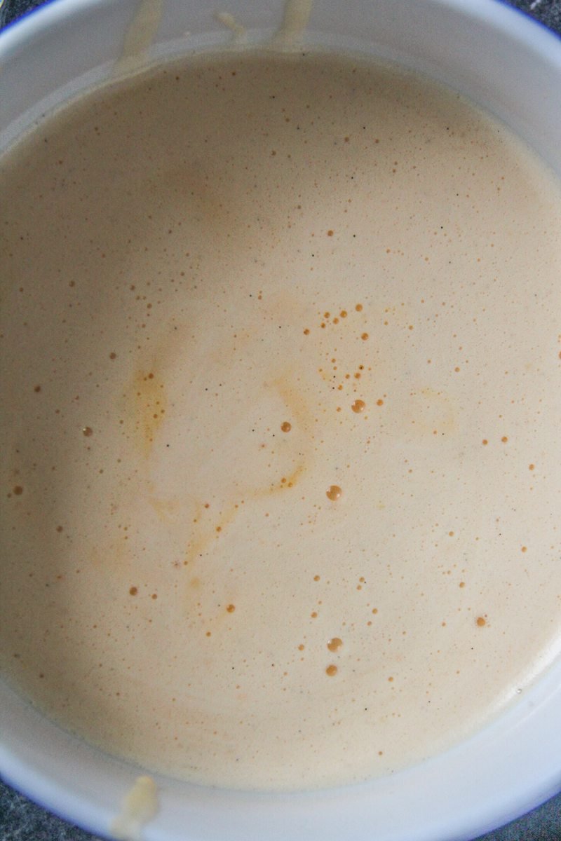 A whipped egg mixture sits in a white ceramic bowl on a dark surface.