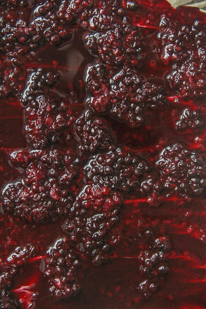 Roasted blackberries lightly mashed sit in their juices on parchment paper.