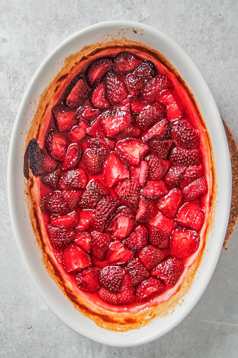 Roasted cut strawberries sit in white ceramic oval dish on a gray dish.