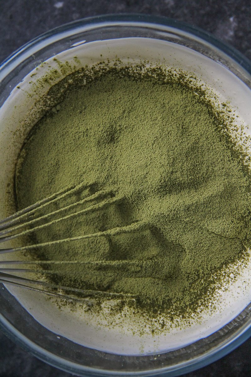 Matcha powder sits on whipped cream in a glass bowl on a dark surface.