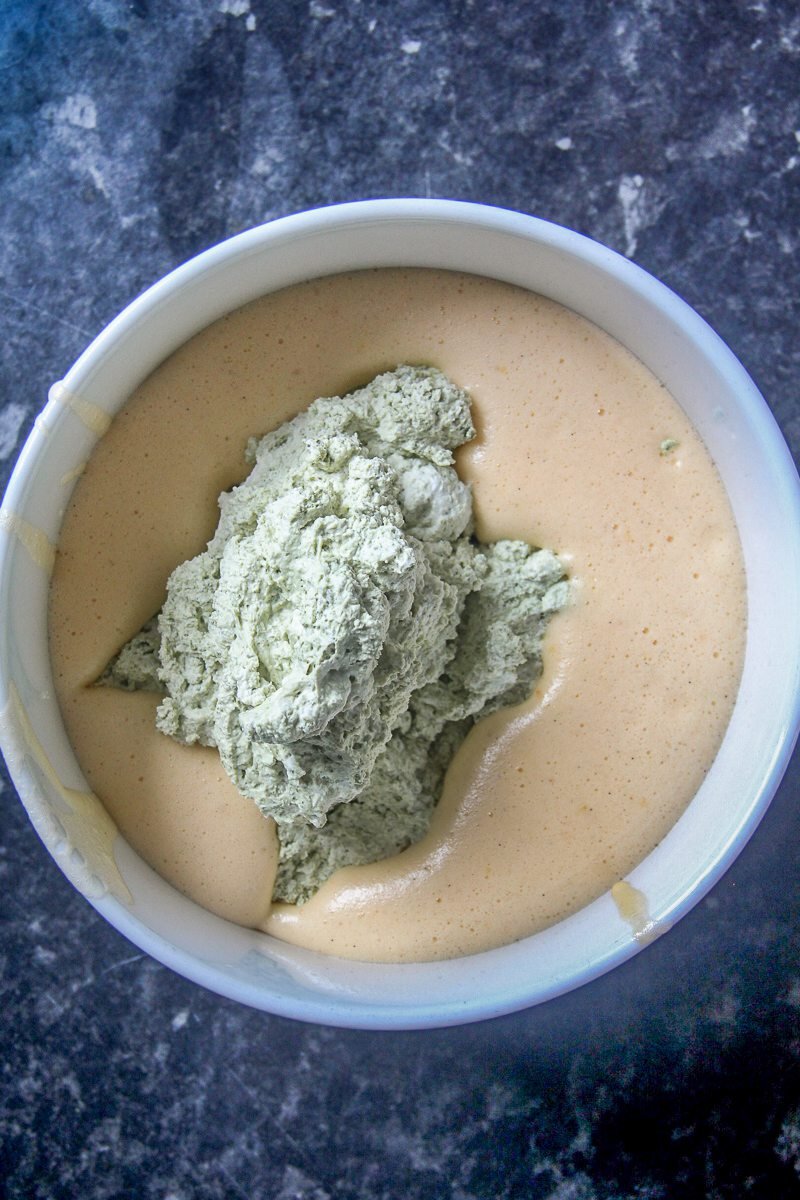 Whipped matcha cream sits in a whipped egg mixture in a white ceramic bowl on a dark surface.