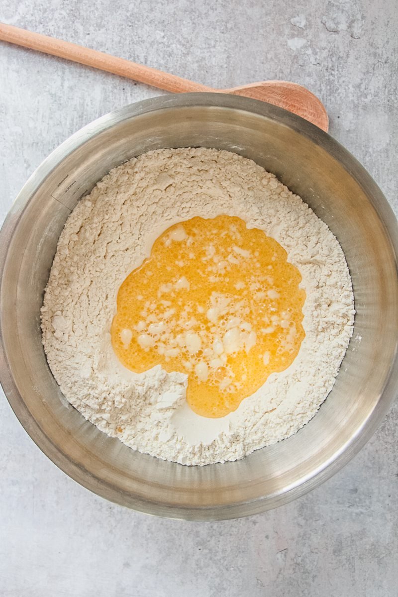 Melted butter sits in the center of a dry mixture in a stainless steel bowl on a gray surface.