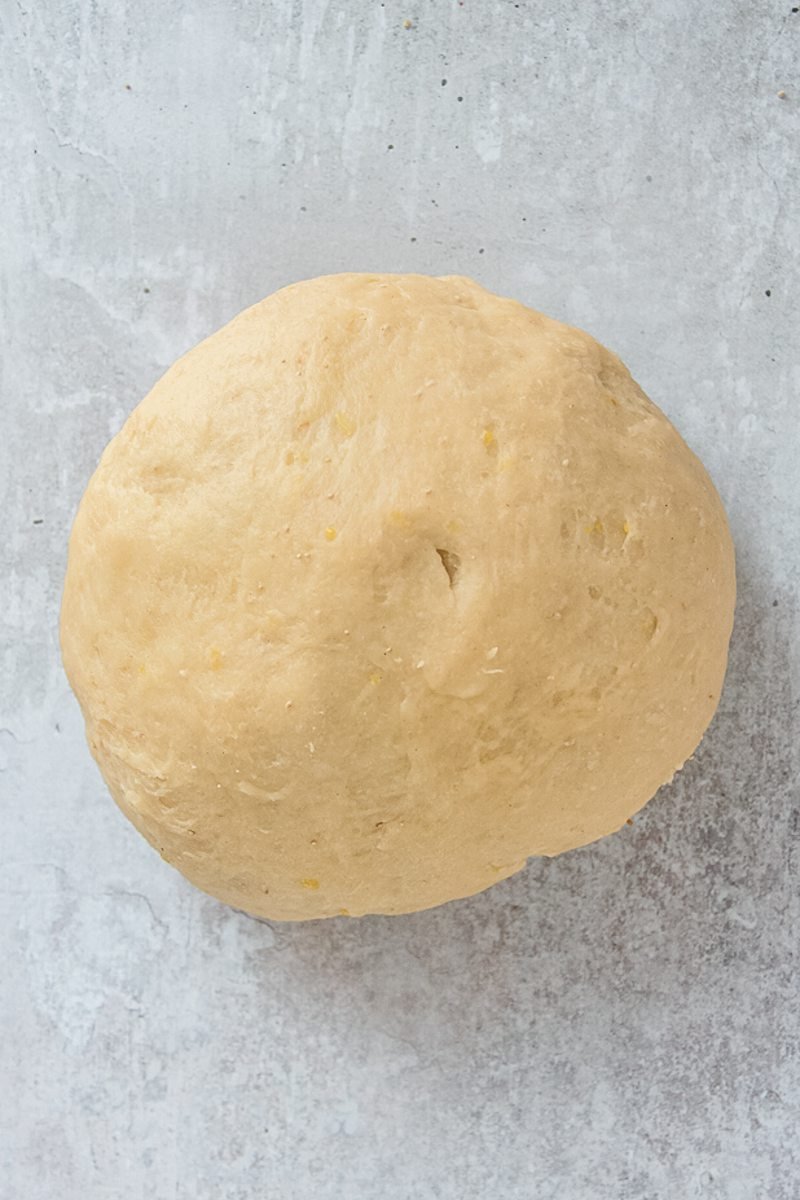 A ball of risen dough sits on a gray surface.