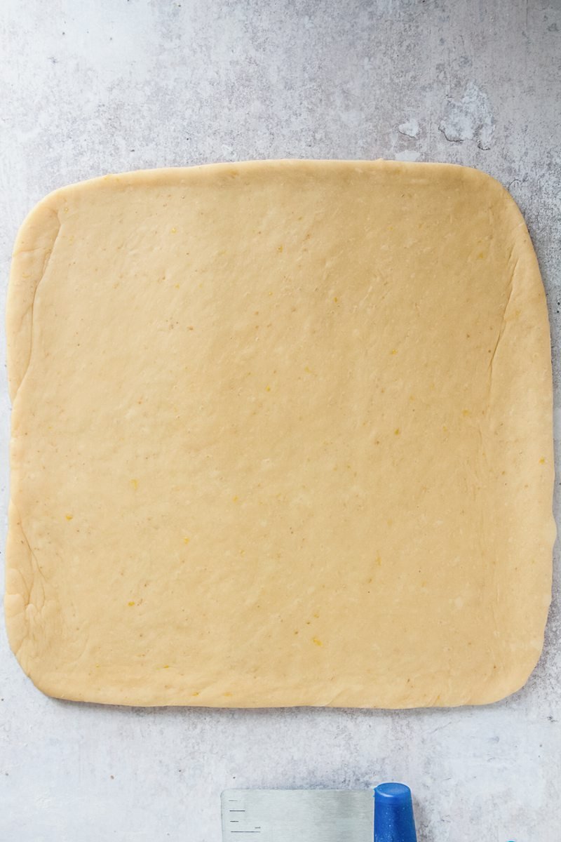 A square of dough sits on a gray surface after being rolled out to ¼ inch thickness.