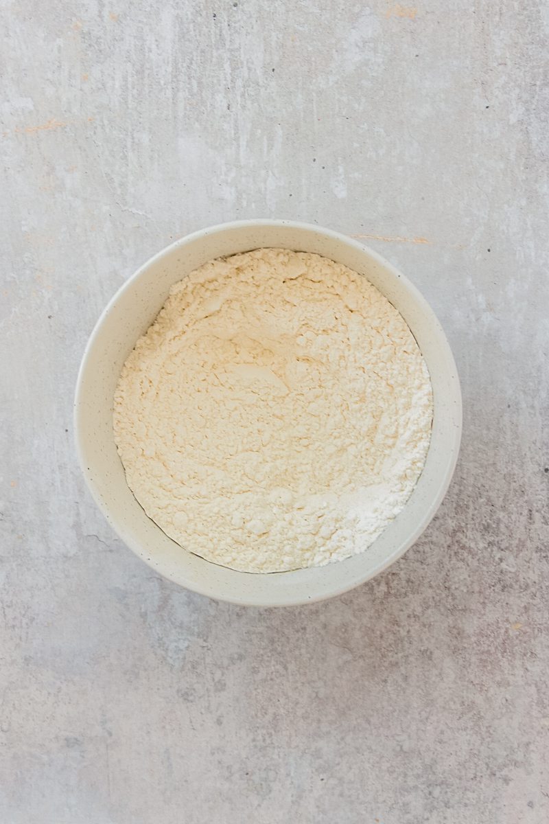 Dry ingredients sit stirred in a white ceramic bowl on a gray surface.