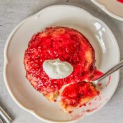 An Irish Jam pudding sits on a fluted white ceramic plate on a gray surface with a spoonful of pudding resting on the plate.