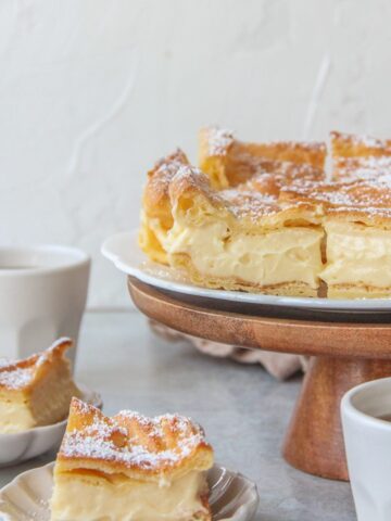 A close up of Karpatka slices on a cake stand with a custard filling.