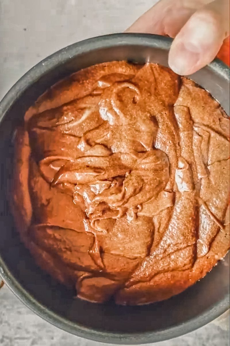 An unbaked chocolate cake sits in a metal round cake tin above a gray surface.