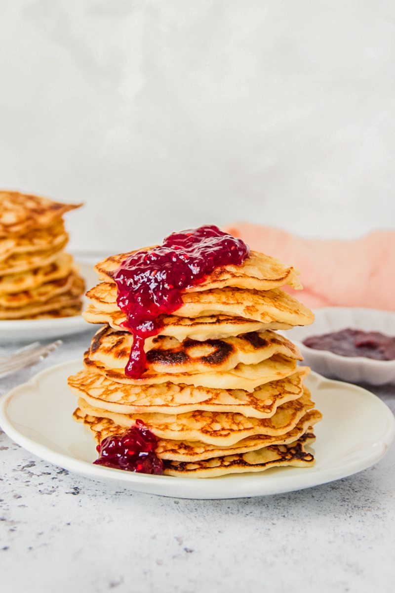 A stack of rice pudding pancakes sits on a white ceramic plate with a thick glob of jam rolling off the stack.