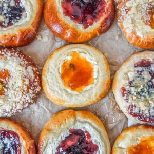 Kolaches with and without streusel toppings sit on parchment paper on a light gray surface.