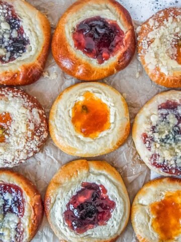 Kolaches with and without streusel toppings sit on parchment paper on a light gray surface.