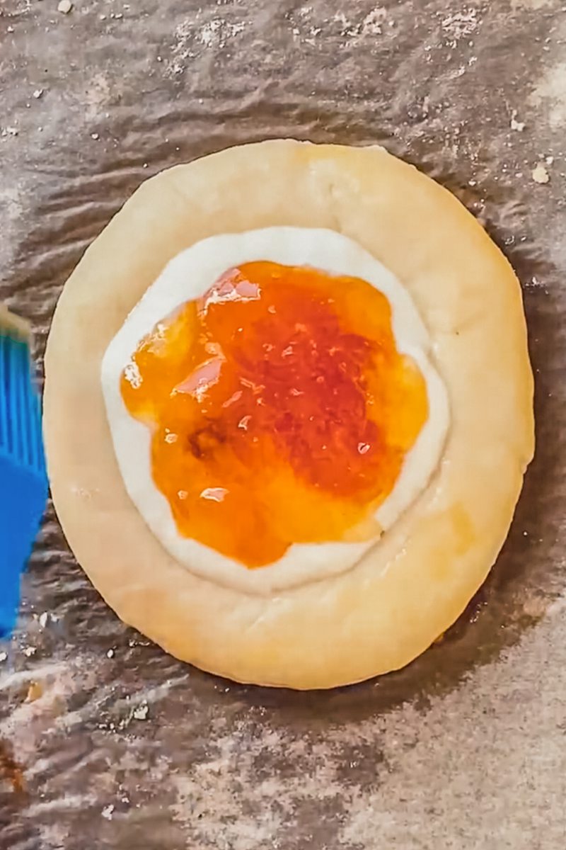 Unbaked kolache is brushed with an egg wash on a baking tray on parchment paper.