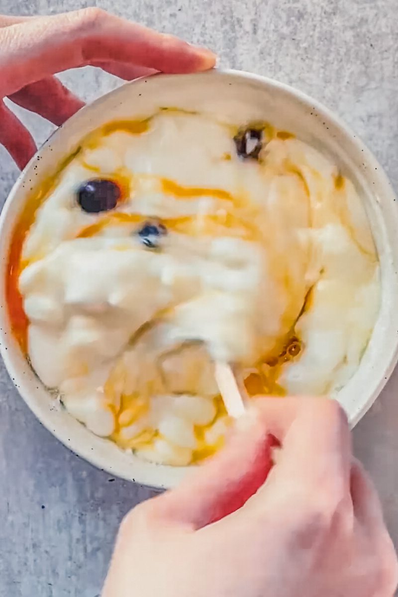 Kolache cream cheese filling is stirred in a white ceramic bowl on a gray surface.