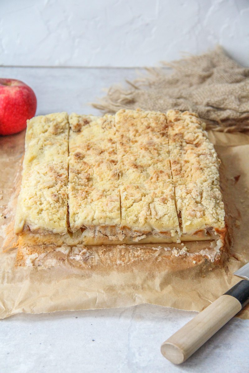 Latvian Apple Bars sits on parchment paper on a gray surface.