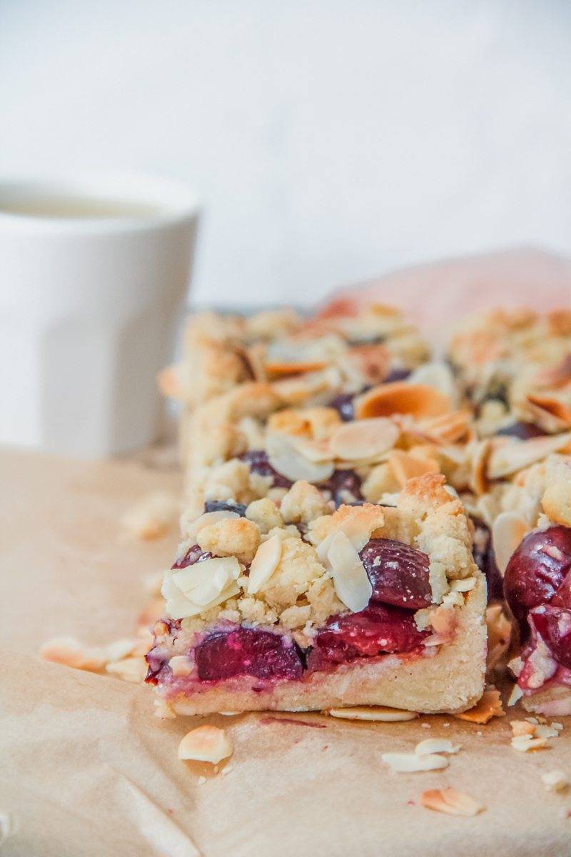 A close up of a slice of Latvian Cherry Crumb cake sits beside the remaining cake on parchment paper.
