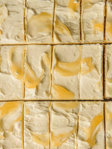 A close up of lemon cookie bars with buttercream frosting and swooshes of lemon curd sit sliced up.