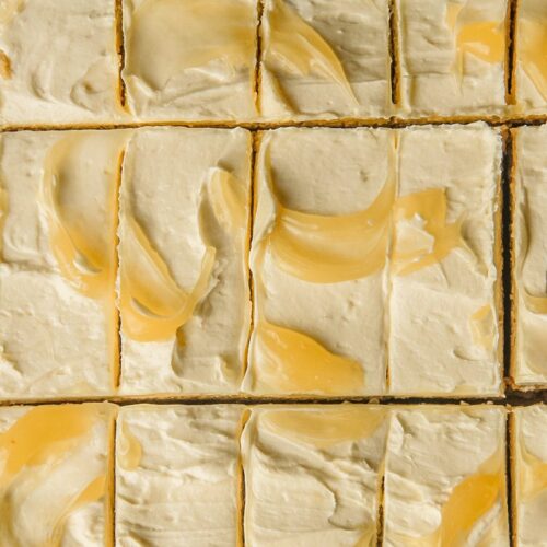 A close up of lemon cookie bars with buttercream frosting and swooshes of lemon curd sit sliced up.