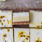 A close up slice of lime and passionfruit bars sits on it's side with the three layers visible with the remaining bars surrounding it on parchment paper.