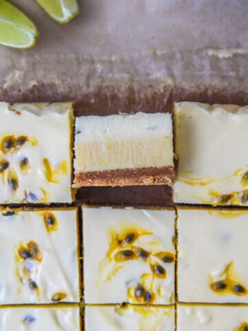 A close up slice of lime and passionfruit bars sits on it's side with the three layers visible with the remaining bars surrounding it on parchment paper.