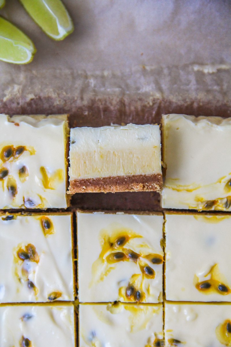 A close up slice of lime and passionfruit bars sits on it's side with the three layers visible with the remaining bars surrounding it on parchment paper.