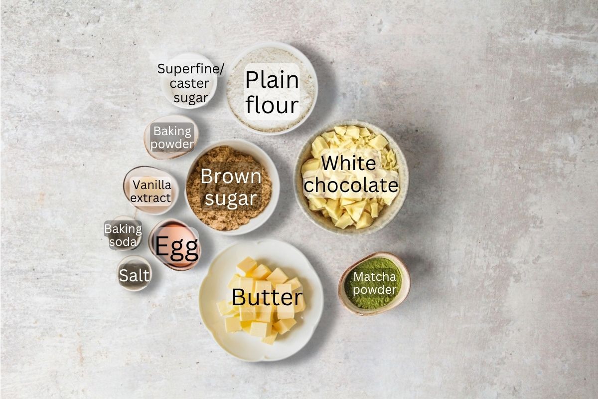 Ingredients for Matcha White Chocolate Cookies sit in bowls on a gray surface.