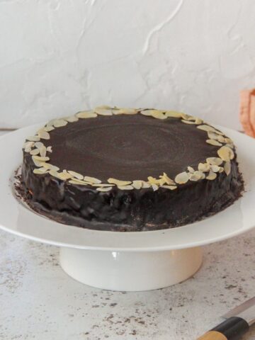 Mazarinkage - Danish Mazarin Cake sits on a white cake stand on a light gray surface.