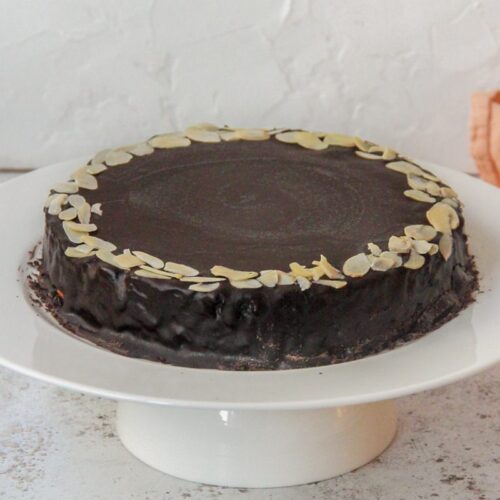 Mazarinkage - Danish Mazarin Cake sits on a white cake stand on a light gray surface.