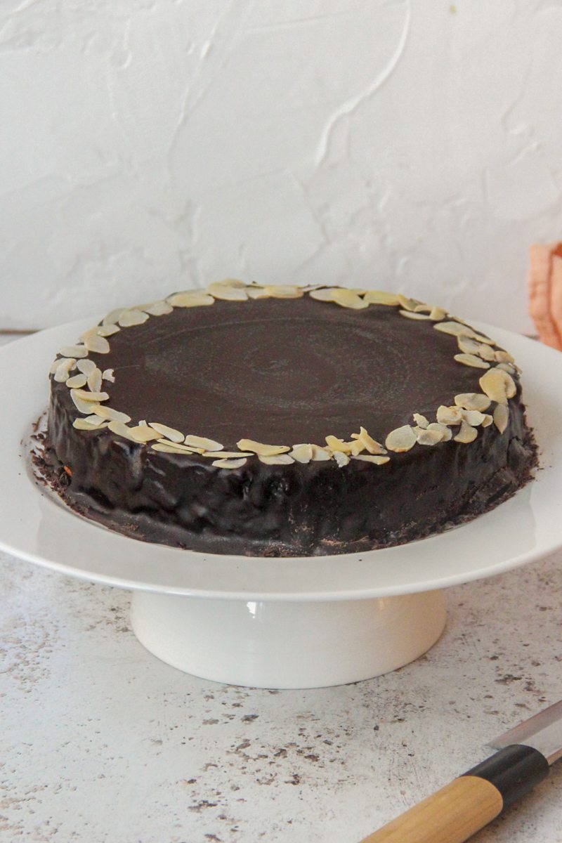 Mazarinkage - Danish Mazarin Cake sits on a white cake stand on a light gray surface.