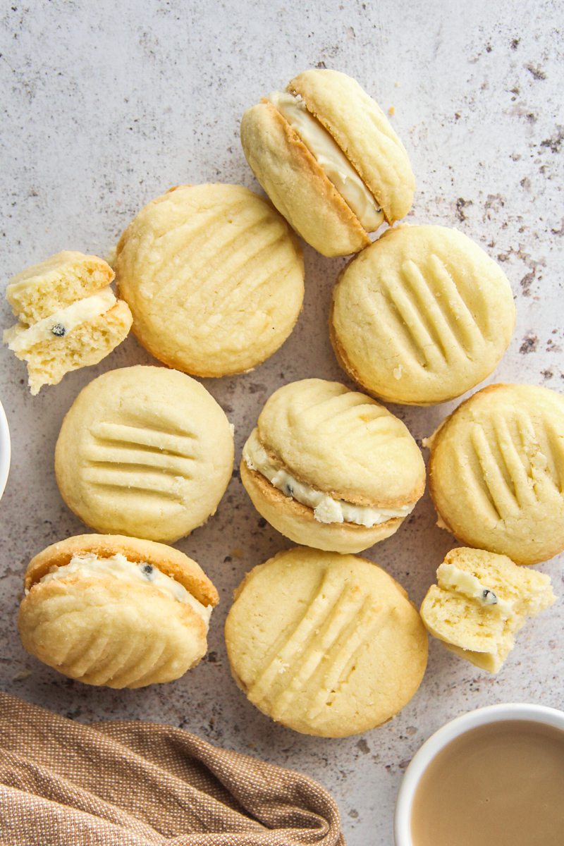 Melting Moments lay on a light gray surface with a few on their side to show off the passionfruit icing with a brown cloth beside.