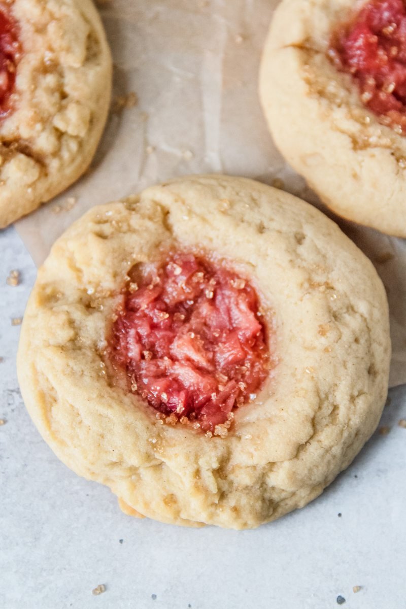 A peach muffin cookie sits beside other cookies on a light grey surface.