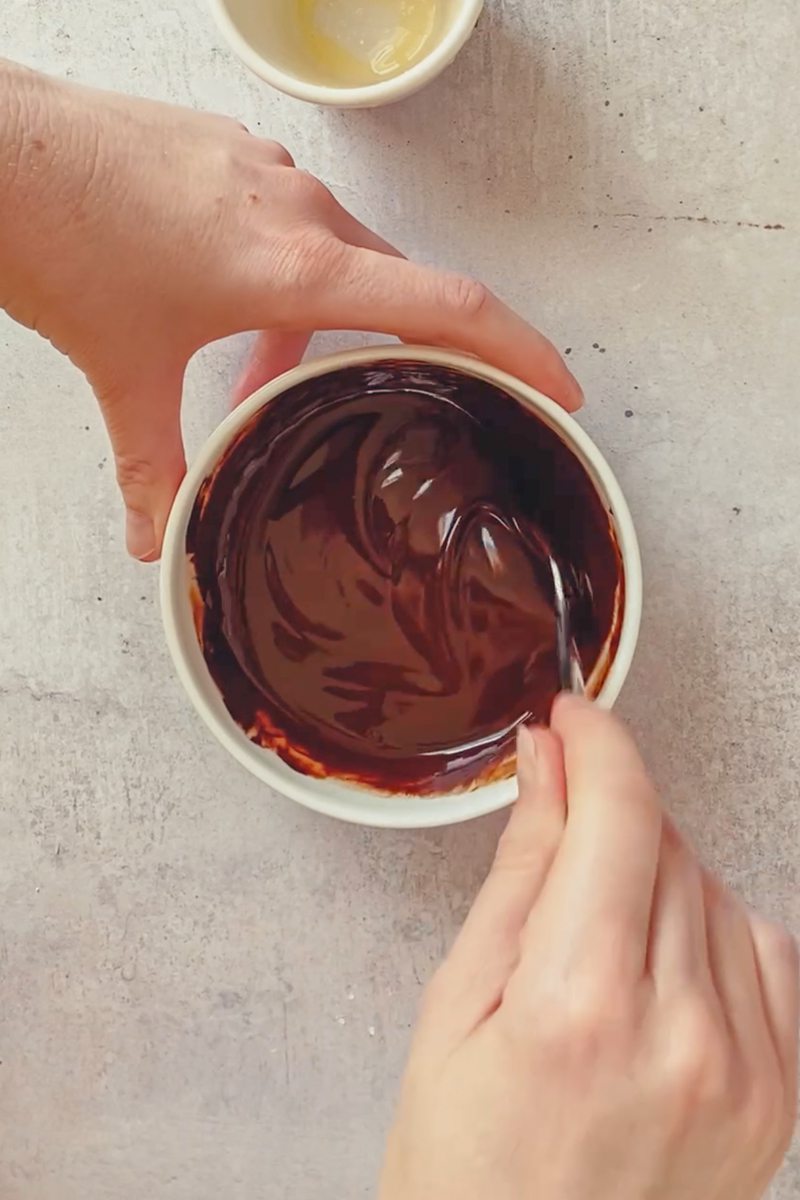 Chocolate and melted butter is stirred in a white ceramic bowl on a gray surface.