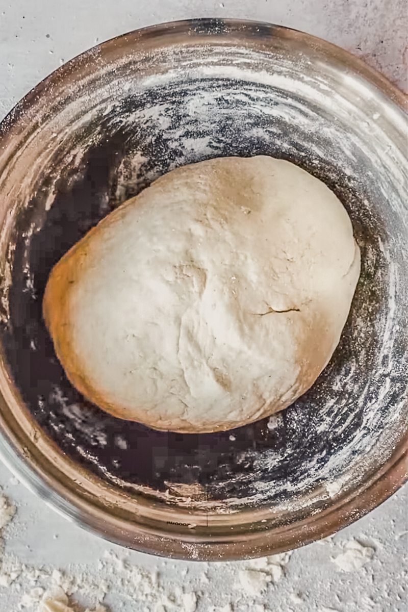 Native American Masa Bread dough sits in a floured stainless steel bowl on a floured gray surface.