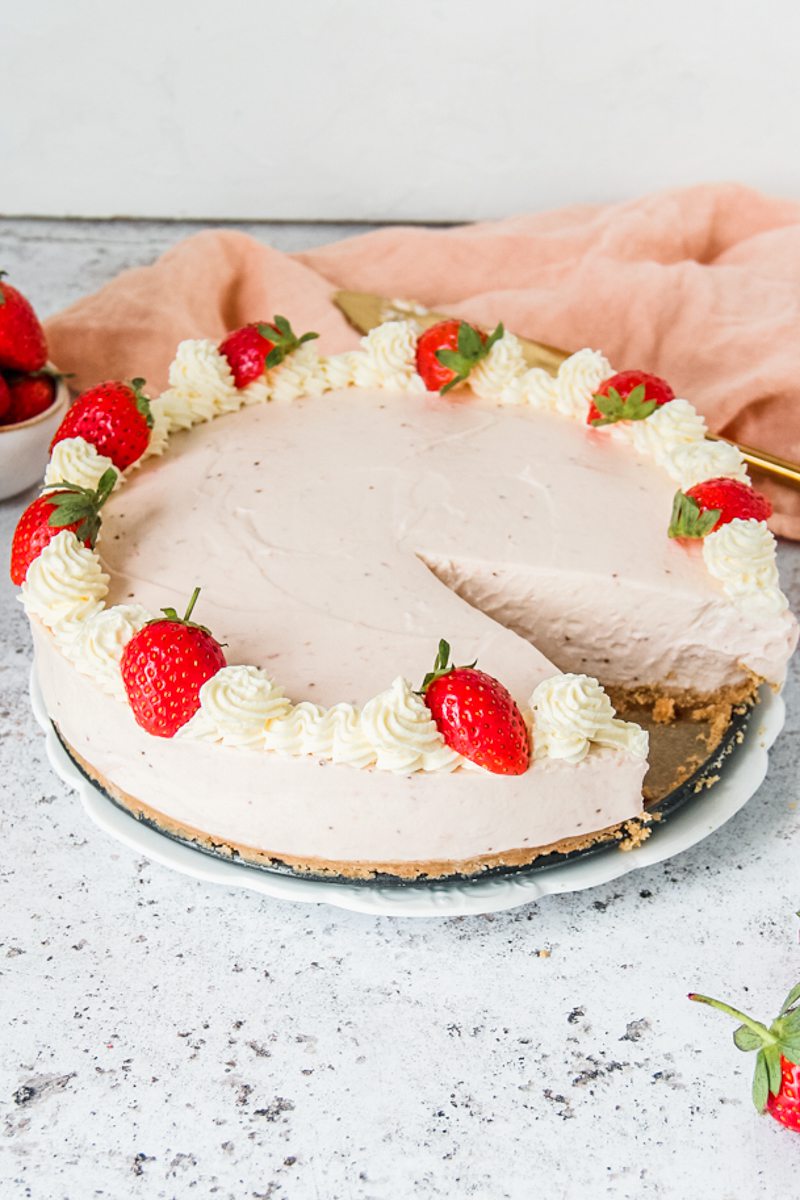 No bake strawberry cheesecake sits on a white plate on a light gray surface with a slice cut to show the light creamy center.